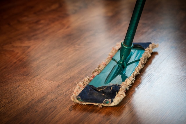 green floor duster being used on a dark hardwood flooring